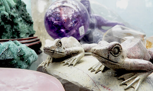 Carved stone twin frogs with amethyst sphere and green minerals in background