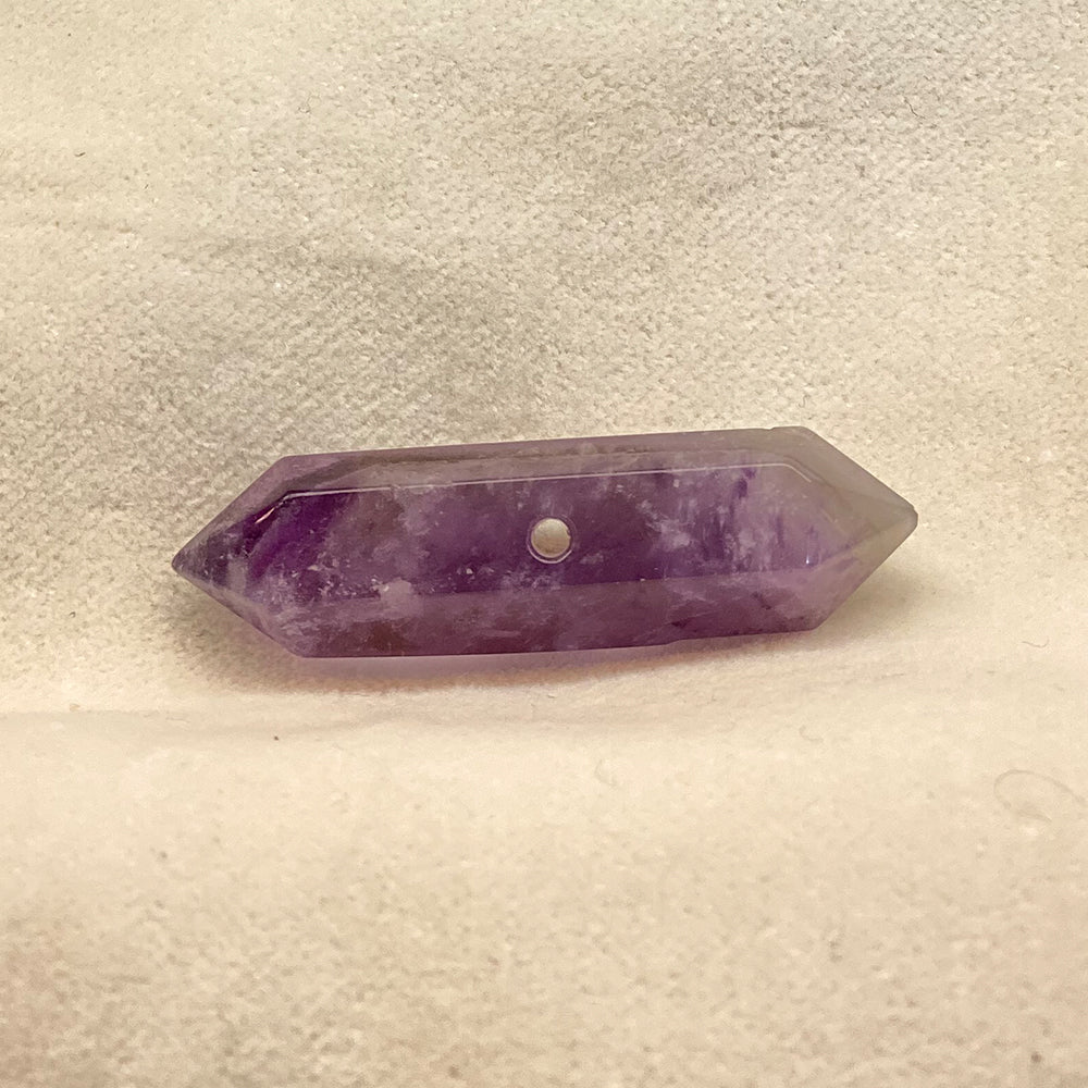 Double-terminated Amethyst Crystal bead. Cut and polished bead with hole in various places for stringing. Varied shades of translucent purple with opaque streaks.Size: variable, from 1 to 1 1/2 inches.